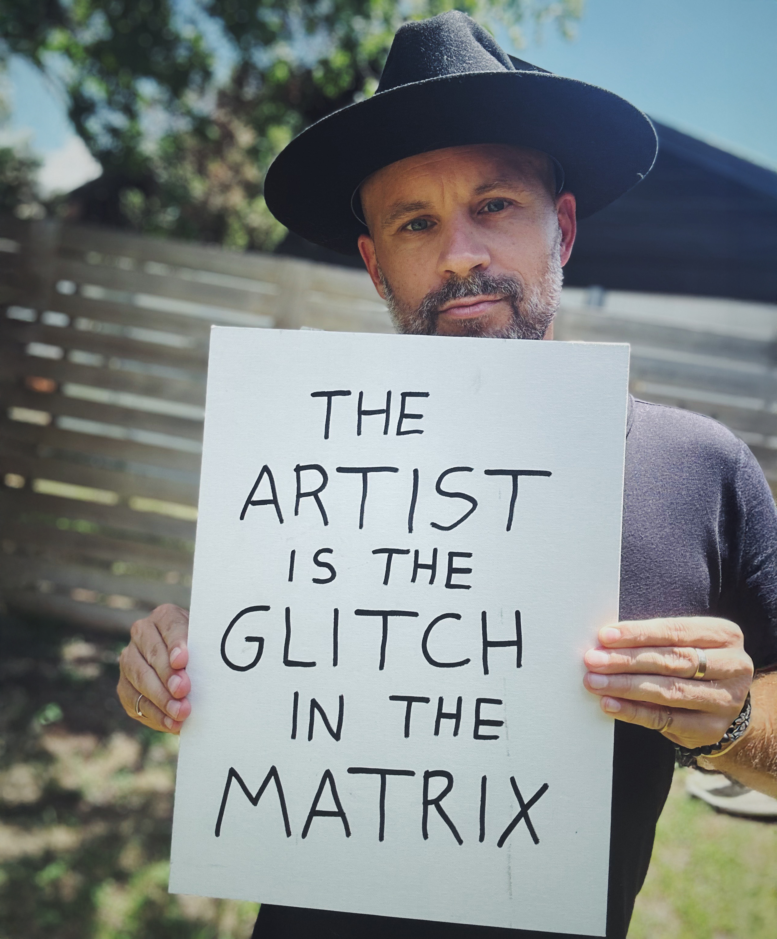 James McCrae holding a sign: The artist is the glitch in the matrix